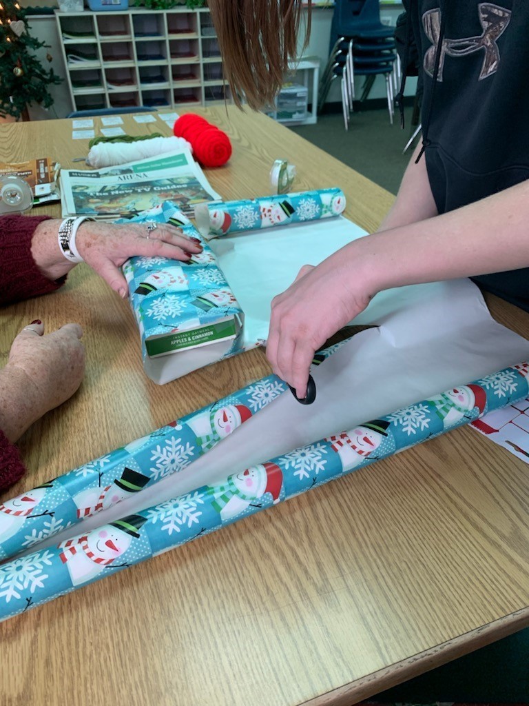 student cutting wrapping paper while staff hold the gift in place